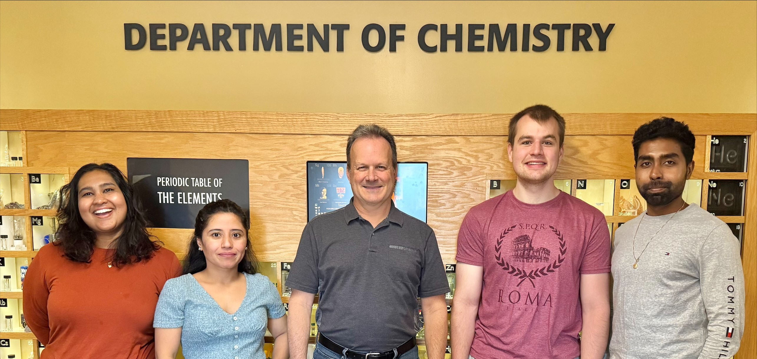 group photo of May2025 Gillan group in front of interactive periodic table